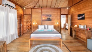 A wooden room with a bed, bedside table, and a painting of a sunset. - Kuda Laut Boutique Dive Resort (Siladen Island)