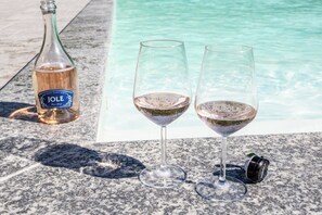 Eine Flasche Jole-Wein und zwei Gläser auf einer Marmorplatte in der Nähe eines Pools.