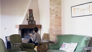 Un salon chaleureux avec une cheminée, des fauteuils verts et une table remplie de livres.