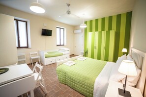 Un dormitorio con una pared verde a rayas, una cama con ropa de cama blanca, un escritorio con una silla, un televisor montado en la pared y un ventilador de techo.