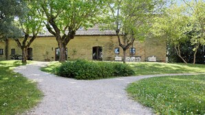 Un bâtiment rustique, avec un chemin de gravier menant à une porte en bois, entouré de verdure et d’arbres.