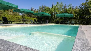 Une piscine à l’eau claire, entourée de chaises longues et de parasols verts.