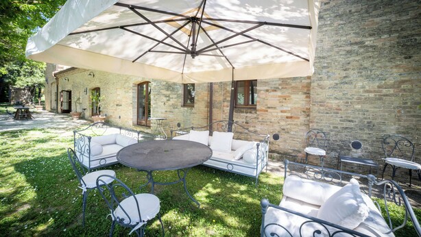 Une terrasse extérieure avec une table ronde, des sièges rembourrés blancs et des chaises en métal.