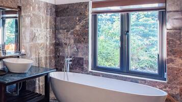 Ein modernes Badezimmer mit freistehender Badewanne, einem großen Fenster und einer Steinwand.