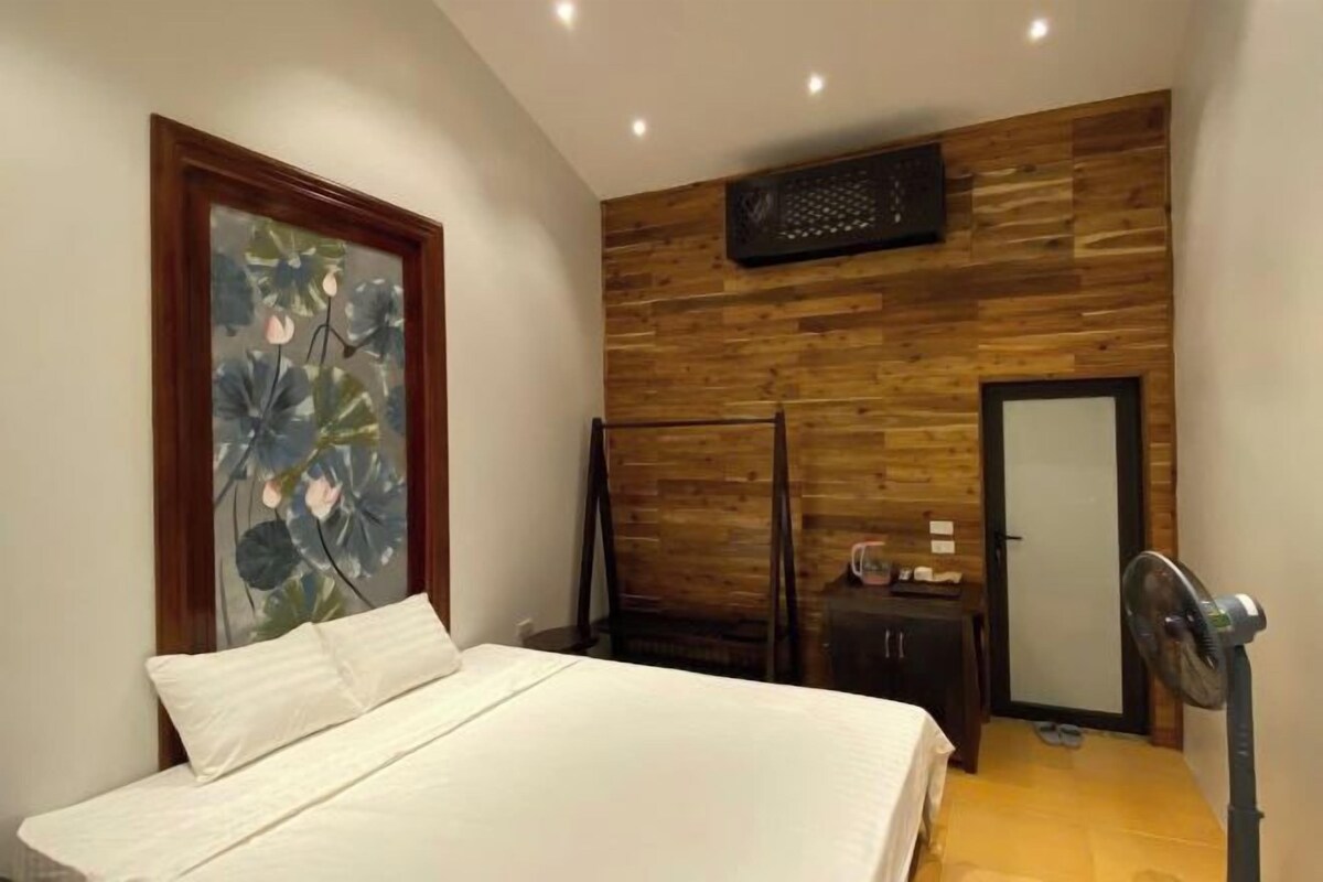 A bedroom with a bed, a wooden wall panel, a door, and a fan.