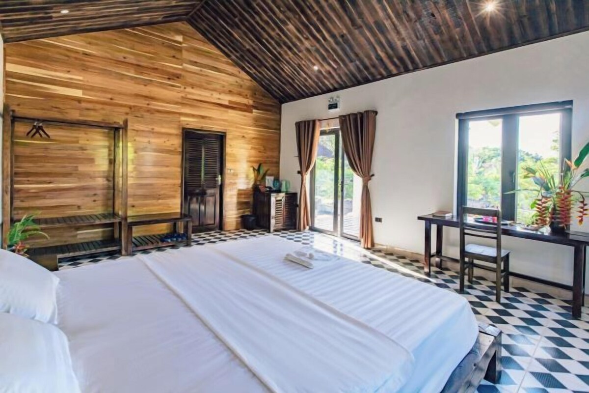 A bedroom with a large bed, wooden ceiling, and a view of the outdoors through a window.