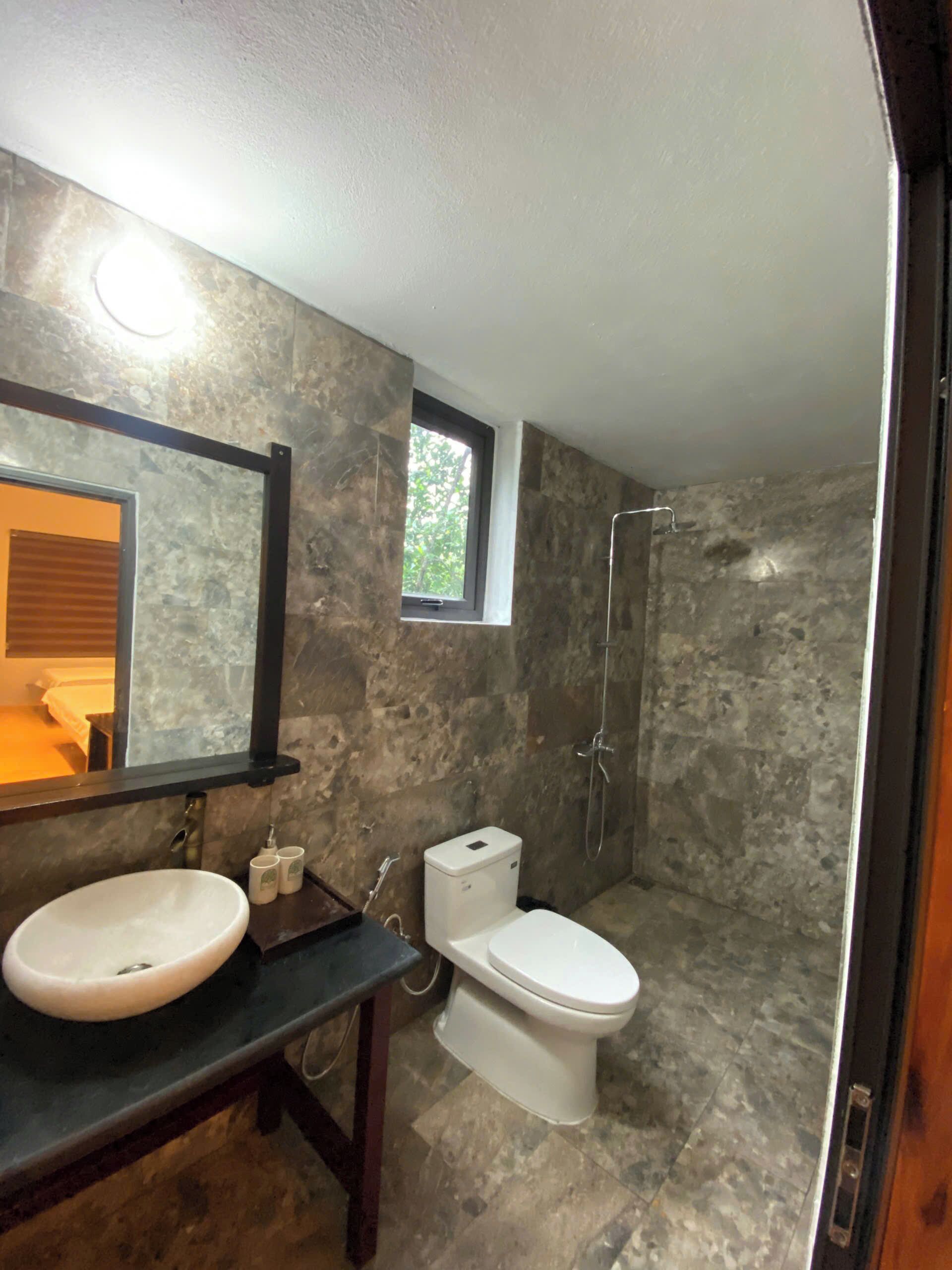 A bathroom with a stone wall, a large mirror, a sink, a toilet, and a shower.