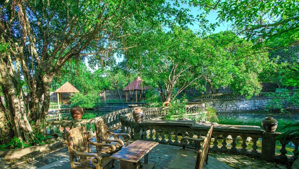 A serene outdoor seating area with stone benches and a wooden table, surrounded by lush greenery and a stone bridge. - Dong Giao Bungalow Ninh Binh (Trung Son)