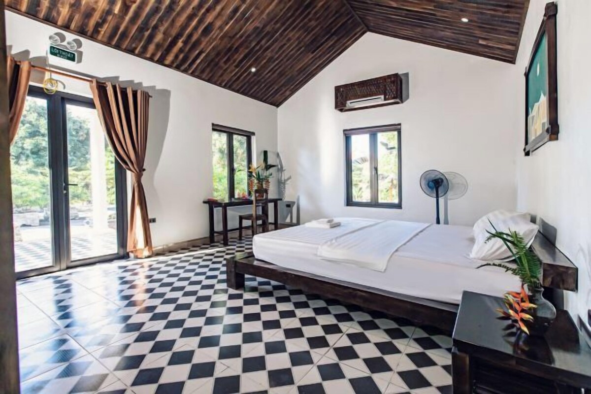 A bedroom with a checkered floor, a bed, a desk, and a fan.