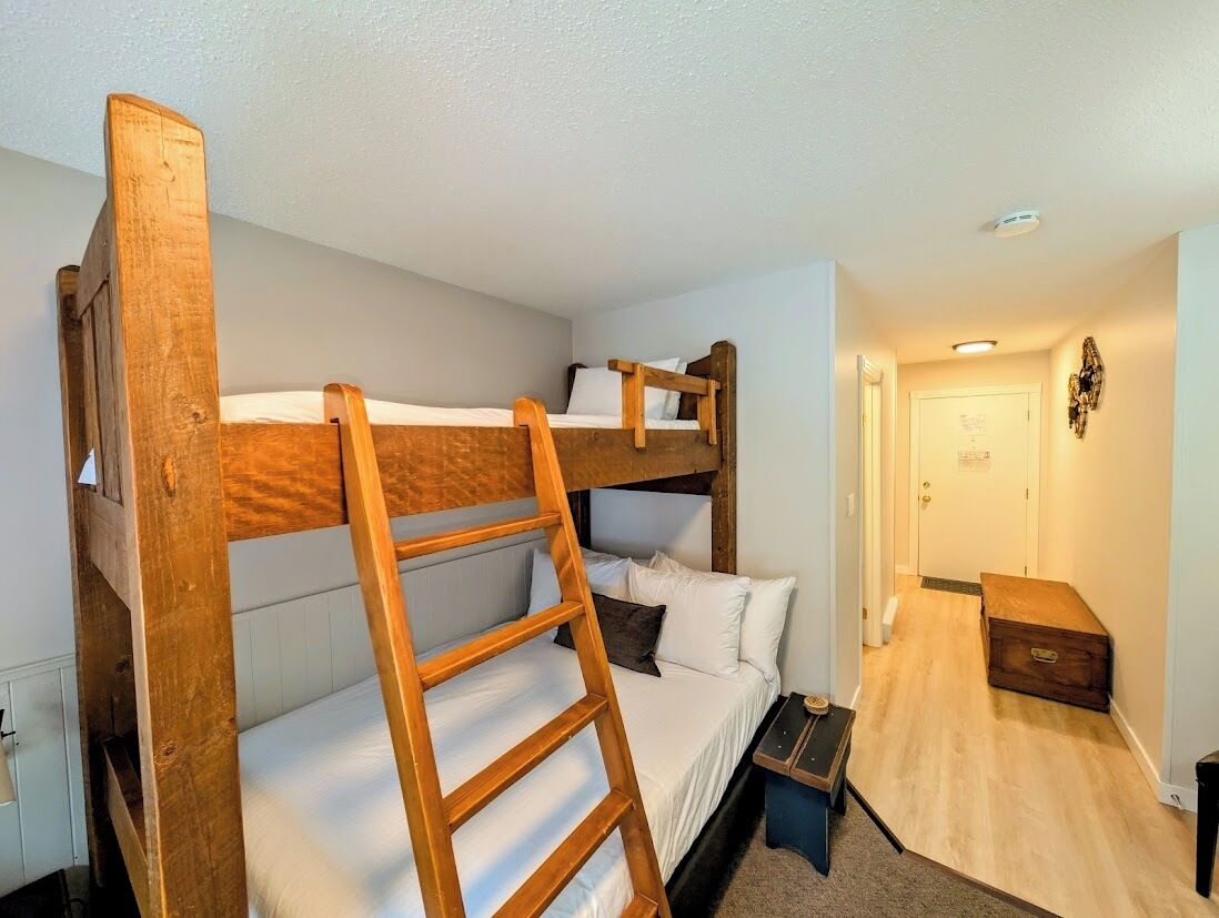 A bunk bed room with a wooden ladder, a bedside table, and a small chest of drawers.
