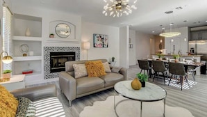 A modern living room with a fireplace, a dining area, and a kitchen.