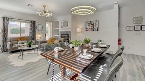 A modern living room with a dining area, featuring a wooden dining table, leather sofas, and a chandelier.