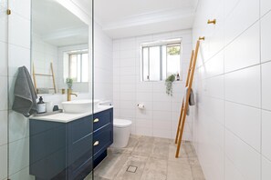 Une salle de bain moderne avec un mur recouvert de carreaux blancs, un meuble-lavabo bleu foncé, un lavabo blanc et des toilettes.