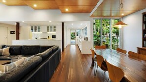 A modern living room with a black leather sofa, a wooden dining table with chairs, and a kitchen in the background. - Cavvanbah Beach Cottage, steps from the beach (Byron Bay)