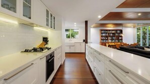 A modern kitchen with white cabinetry, a built-in stove, and a long countertop. - Cavvanbah Beach Cottage, steps from the beach (Byron Bay)