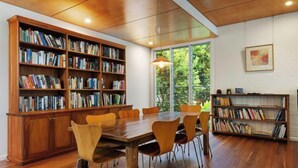 A spacious room with a large wooden table surrounded by chairs, flanked by tall bookshelves filled with books. - Cavvanbah Beach Cottage, steps from the beach (Byron Bay)