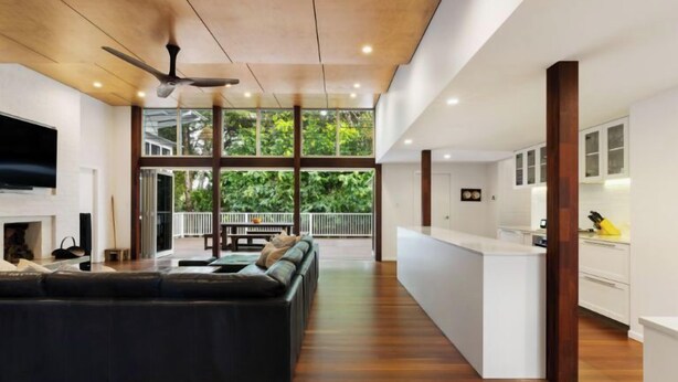 A spacious living area with a large black sofa, a ceiling fan, and a kitchen area with white cabinets. - Cavvanbah Beach Cottage, steps from the beach (Byron Bay)