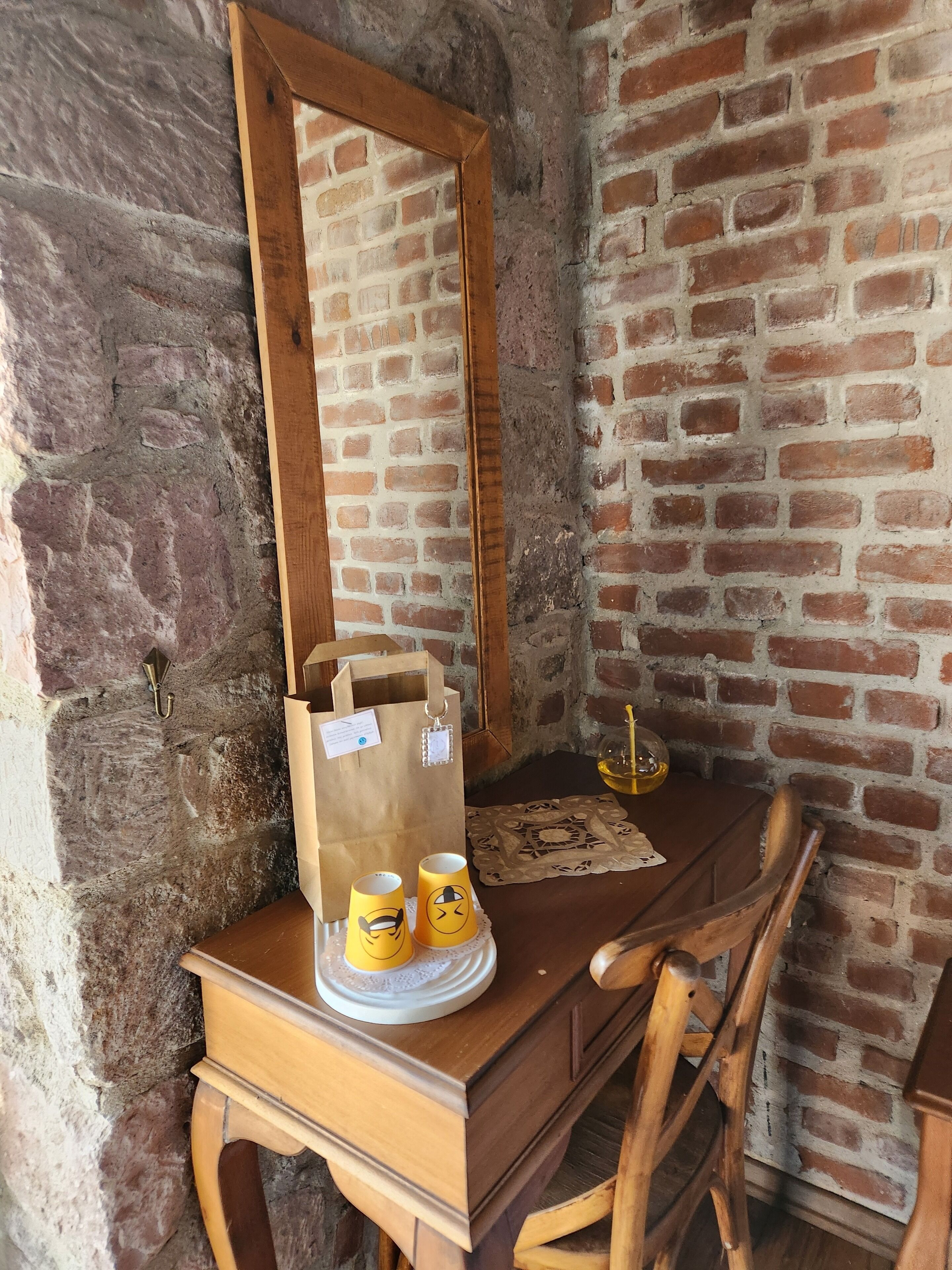 Un escritorio de madera con un espejo, dos tazas, una bolsa de papel y un plato decorativo.
