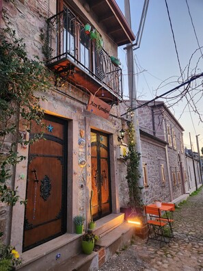 A traditional stone building with a wooden door, a balcony with hanging plants, and a small outdoor seating area. - Azra Konuk Evi (Ayvalik)