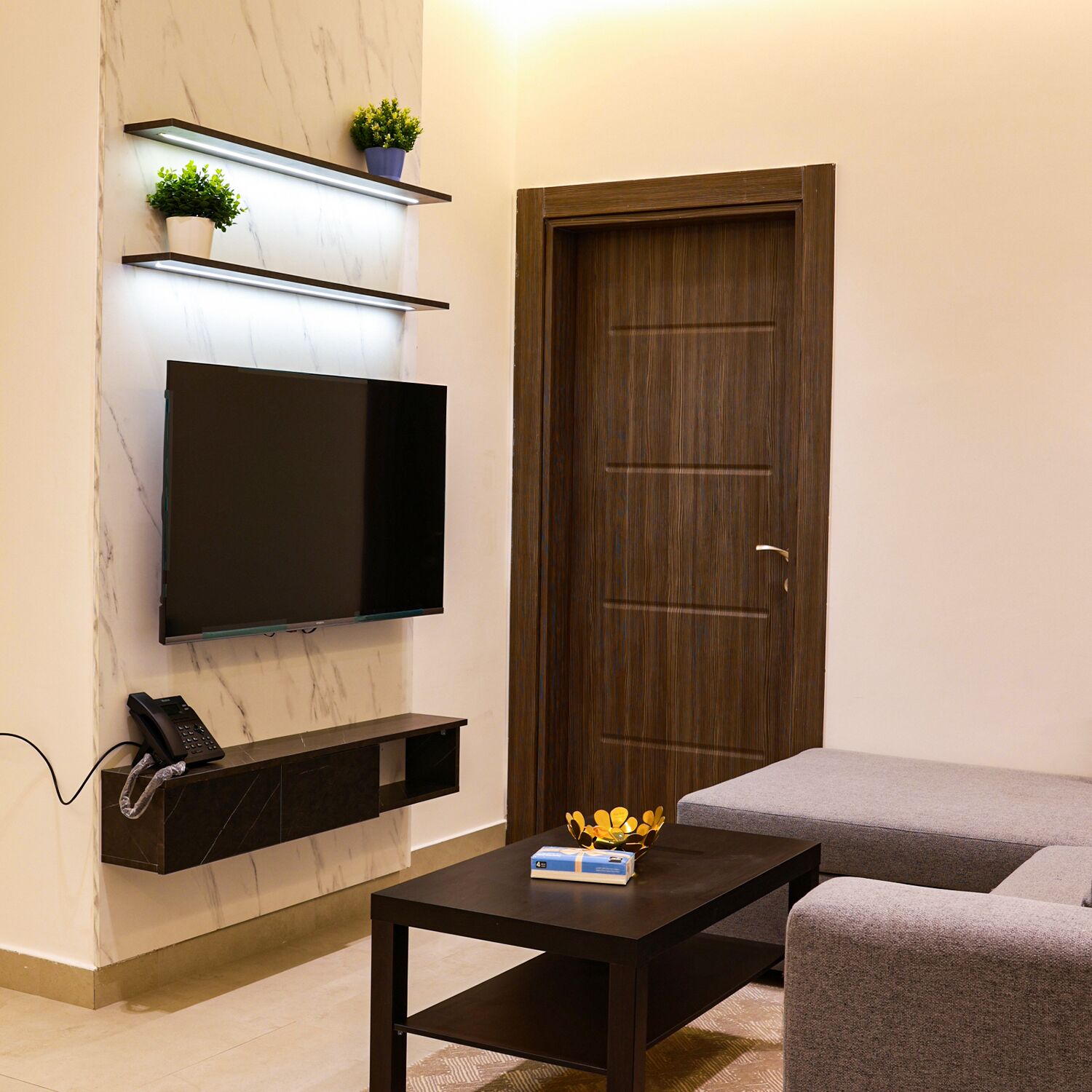 A modern living room with a flat-screen TV mounted on the wall, a wooden door, and a small table with a box on it.