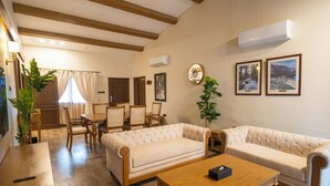 A living room with a sofa, coffee table, and dining area. There are two framed pictures on the wall, an air conditioning unit, and a clock. - K2 Hotel by Green Pak Skardu (Skardu)