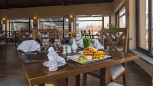 A dining table set with a burger, fries, salad, and a green drink, with chairs and a window view in the background. - K2 Hotel by Green Pak Skardu (Skardu)