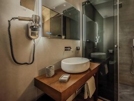 Un bagno moderno con uno specchio grande, un lavandino rotondo e un box doccia in vetro.