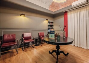 A room with a round table, three leather chairs, a bookshelf, and a red curtain. - Hotiday Palermo Palco Noir (Palermo)