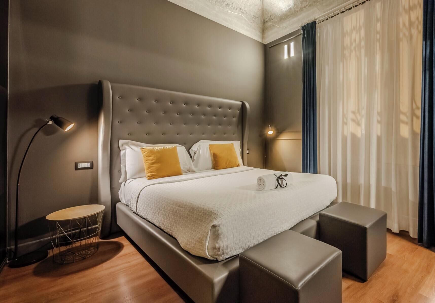A modern bedroom with a large bed, bedside lamps, a round side table, and a bench.