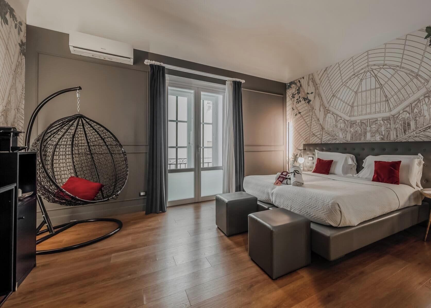 A modern hotel room with a large bed, a hanging chair, and a view of the city through the window.