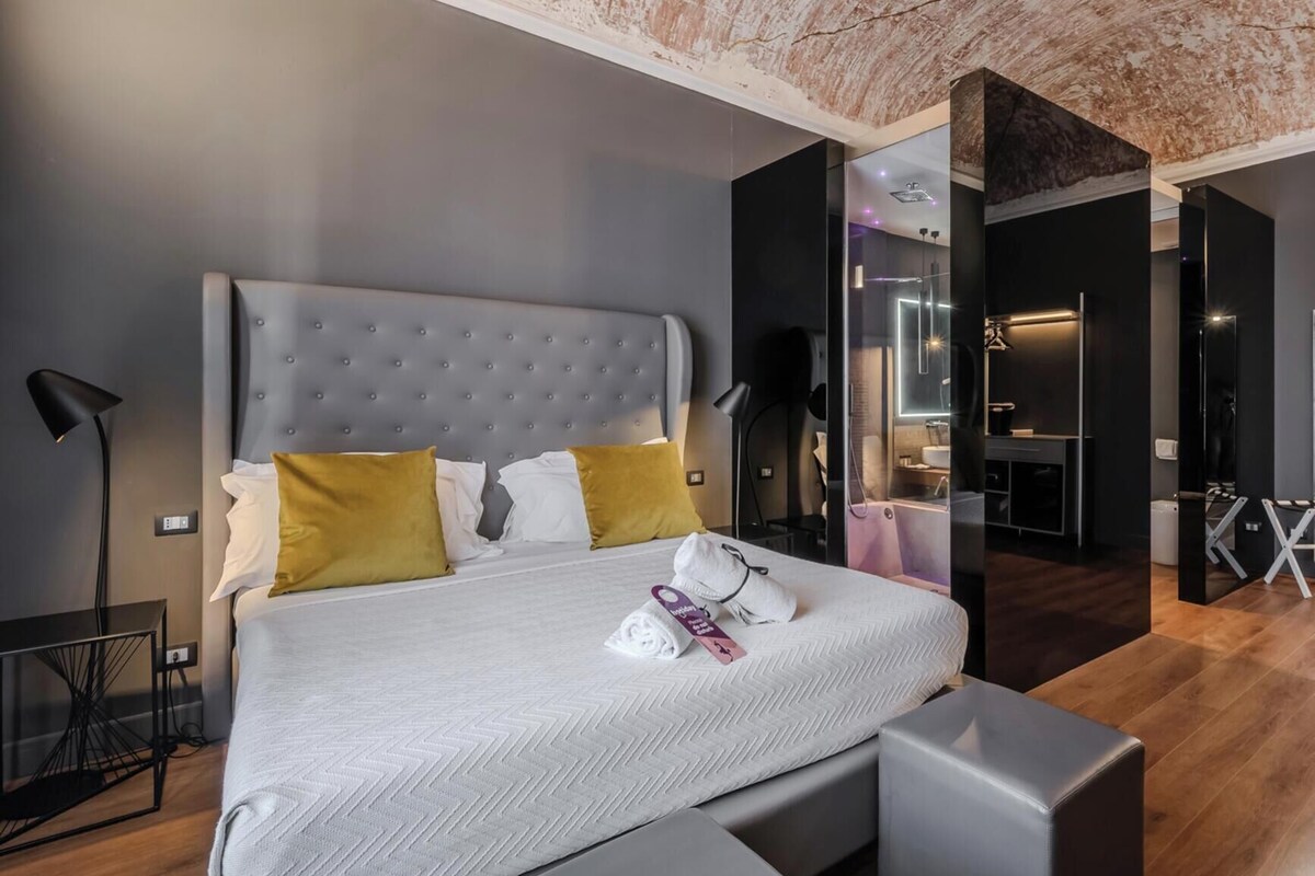 A modern bedroom with a large bed, bedside tables, a desk, and a mirror.