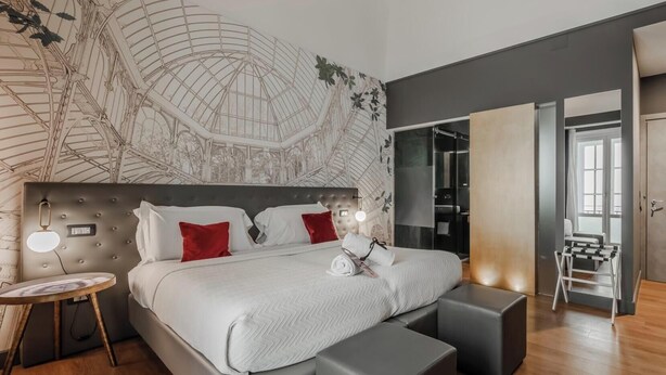 A modern bedroom with a large bed, bedside tables, a wall mural, and a walk-in closet. - Hotiday Palermo Palco Noir (Palermo)
