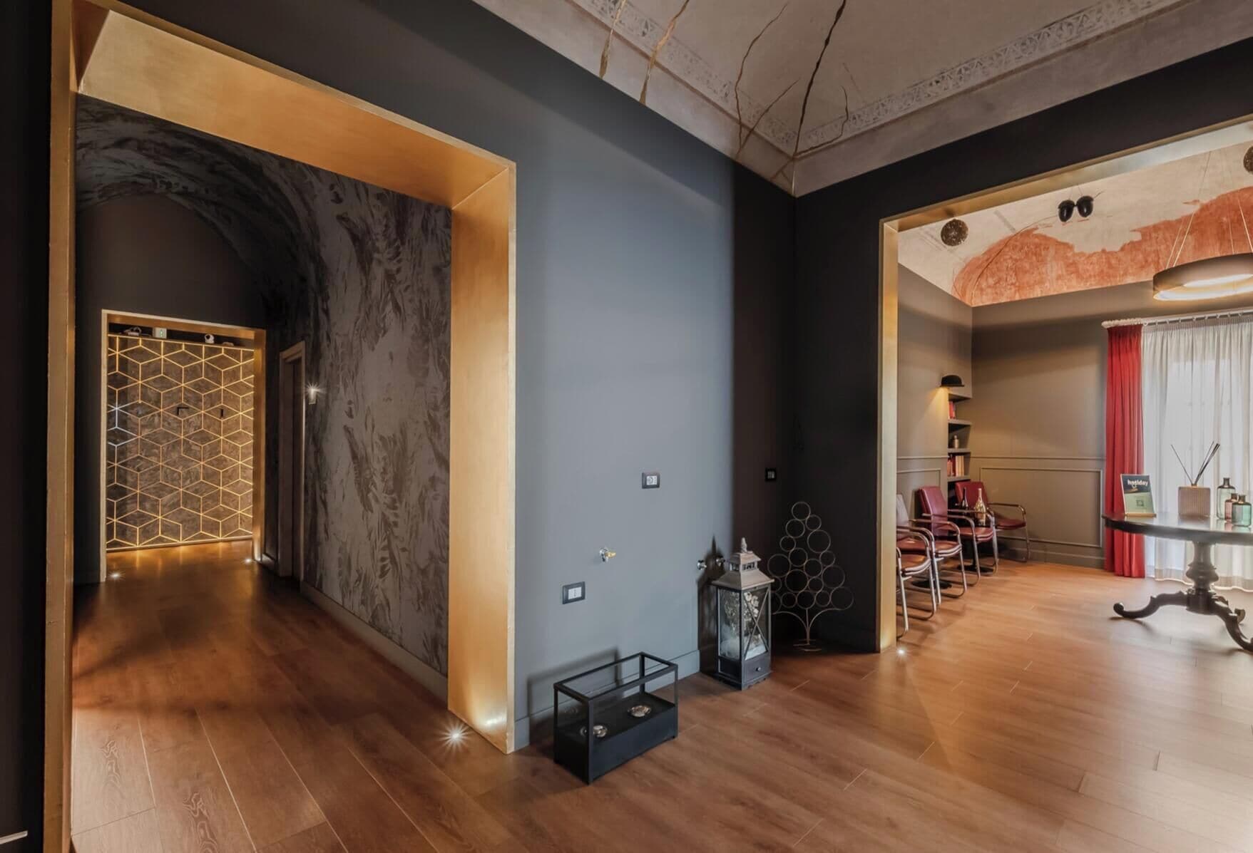 Interior moderno com piso de madeira, design geométrico na parede e área de estar com mesa e cadeiras.
