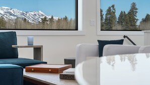 A modern living room with a view of snow-capped mountains and a forest through large windows.