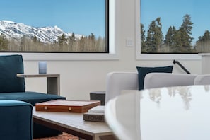 Una sala de estar moderna con vistas a montañas nevadas y un bosque a través de amplios ventanales.