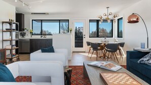 A modern living room with a sofa, a coffee table with a book, and a dining area with chairs and a table.