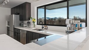 A modern kitchen with dark cabinets, a large window, and a coffee machine.