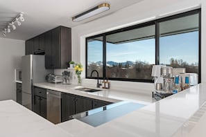 Una cocina moderna con armarios oscuros, un ventanal grande y una cafetera.