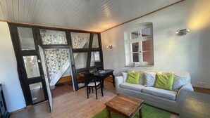 A living room with a wooden floor, a green carpet, a white sofa with green cushions, a wooden coffee table, and a dining area with a black table and chairs.