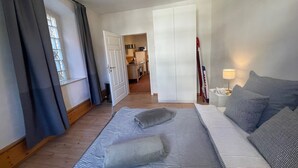 A bedroom with a bed, a nightstand, a lamp, and a view of a kitchen and closet.