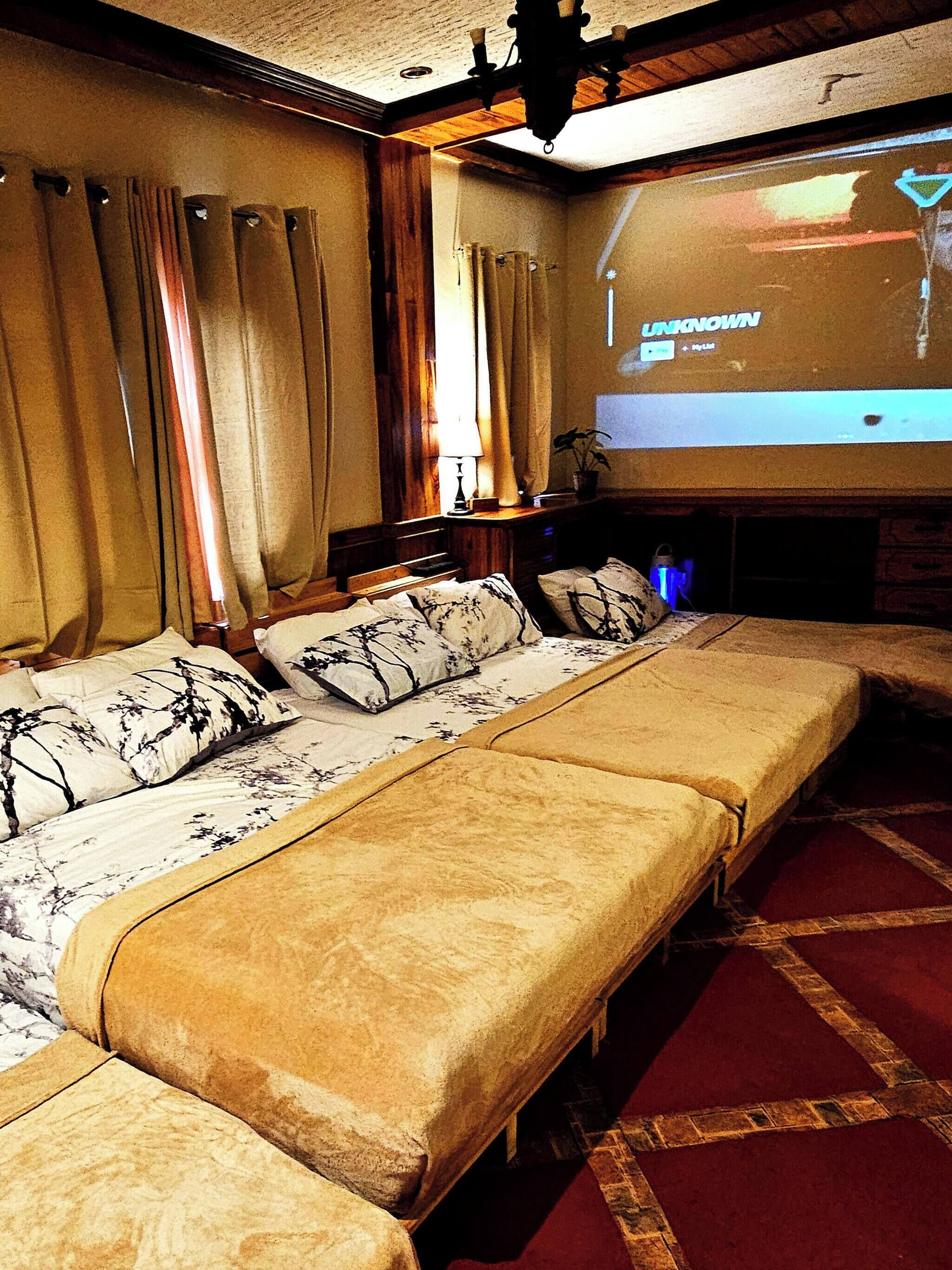 A hotel room with a large bed, a TV screen displaying 'UNKNOWN', and a projector.