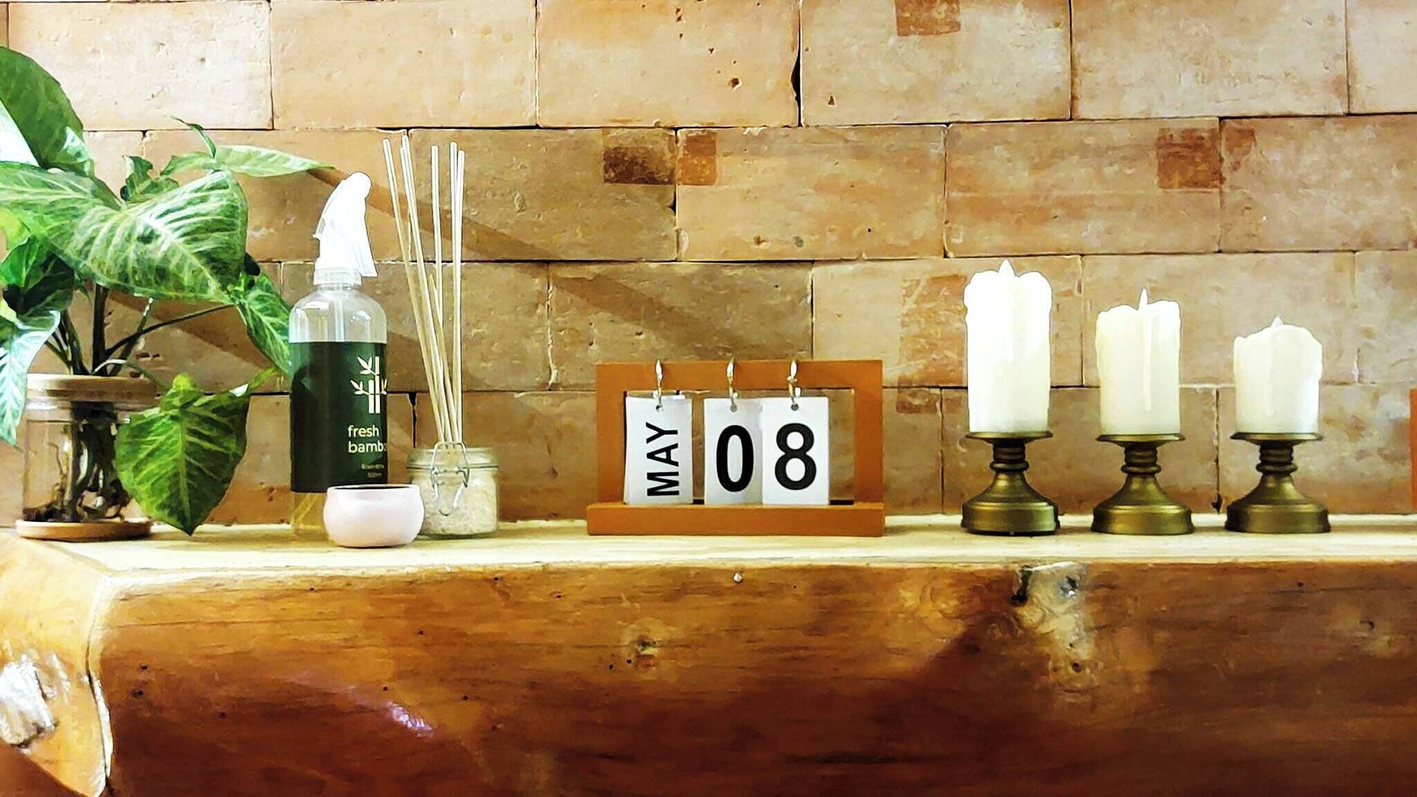 Une étagère en bois avec un calendrier, des bougies, un diffuseur d’huiles essentielles et une plante en pot.