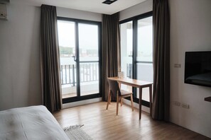 A hotel room with a bed, a desk, and a TV. There are large windows with curtains, and a view of a balcony. - Here It's home (Lyudao)