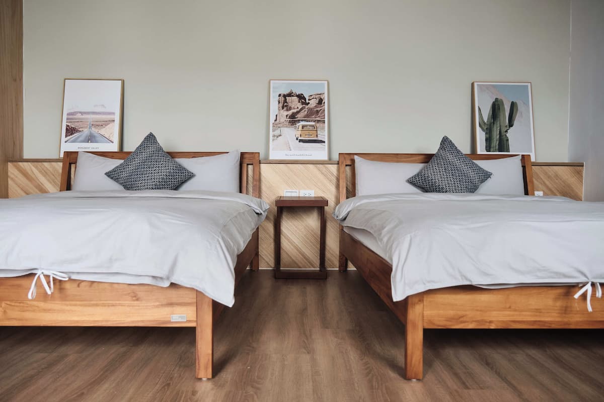 A room with two wooden beds, each with a pillow and a framed picture on the wall.
