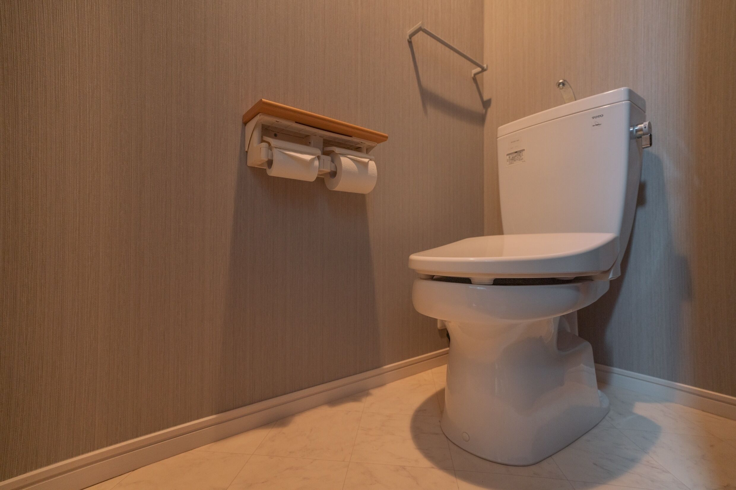 A modern bathroom with a white toilet, a wooden shelf with toilet paper, and a wall-mounted towel rack.