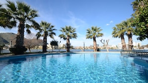 Una piscina azul cristalina rodeada de palmeras y una vista de la ciudad al fondo.