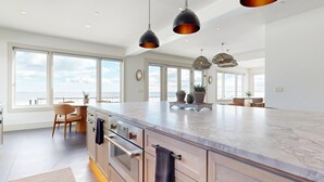 Una cocina amplia con una isla grande, modernas lámparas colgantes y ventanas grandes que ofrecen vistas al océano.