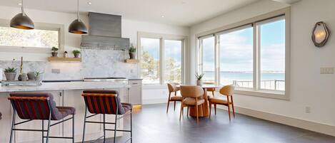A modern kitchen with a large island, bar stools, and a dining area with a view of the sea.