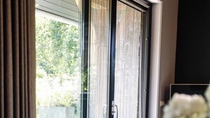 A dining area with a table set for two, a sliding glass door leading to a garden, and a vase with flowers on the table. - Atmospheric luxury holiday home –  spacious garden – 5 minutes from the forest. (Wilbertoord)