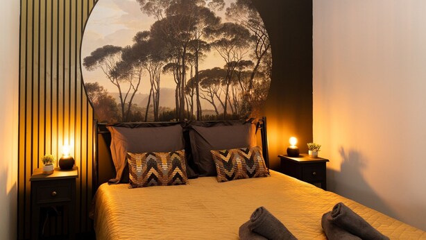 A neatly made bed with a quilted cover, two pillows with a geometric pattern, and two rolled towels on the bed. - Atmospheric luxury holiday home –  spacious garden – 5 minutes from the forest. (Wilbertoord)